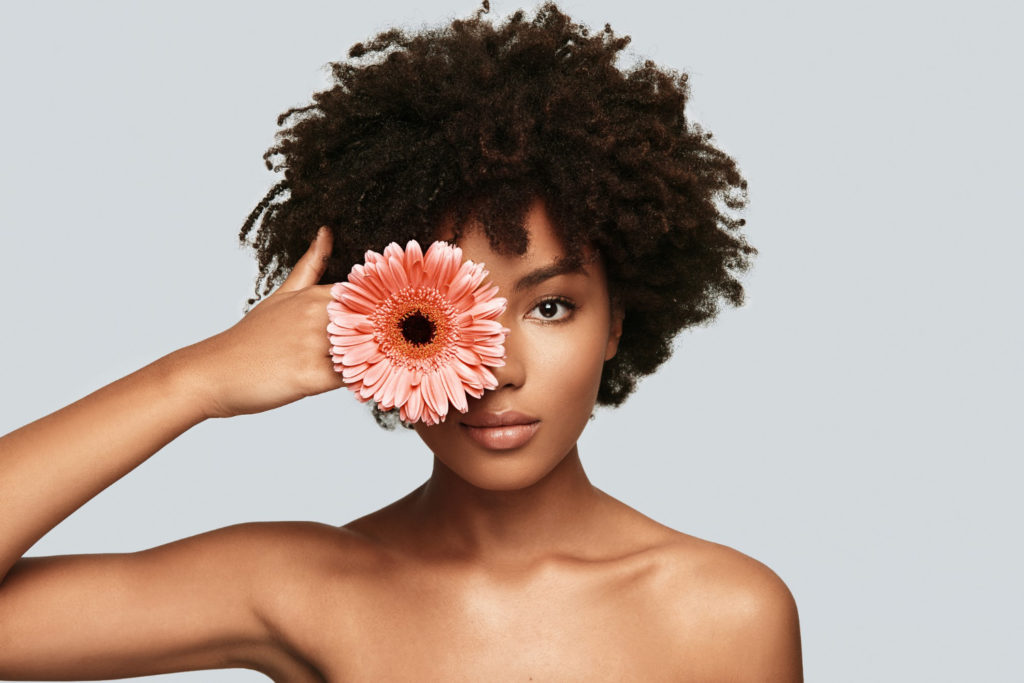 beautiful as flower attractive young african woman looking camera covering eye with flower while standing against grey background