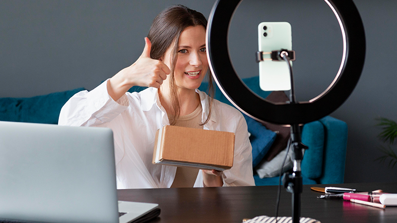  A woman recording a video review, giving a thumbs-up to the camera, highlighting the effectiveness of personal customer testimonials in e-commerce marketing.
